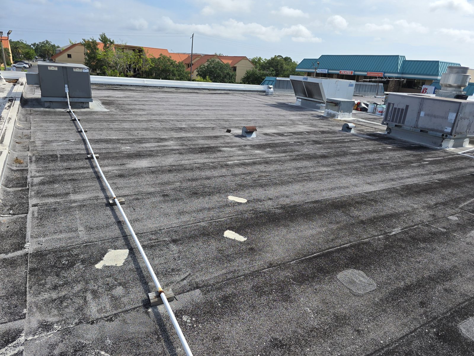 Aged and soiled commercial flat roof with rooftop units in place before restoration