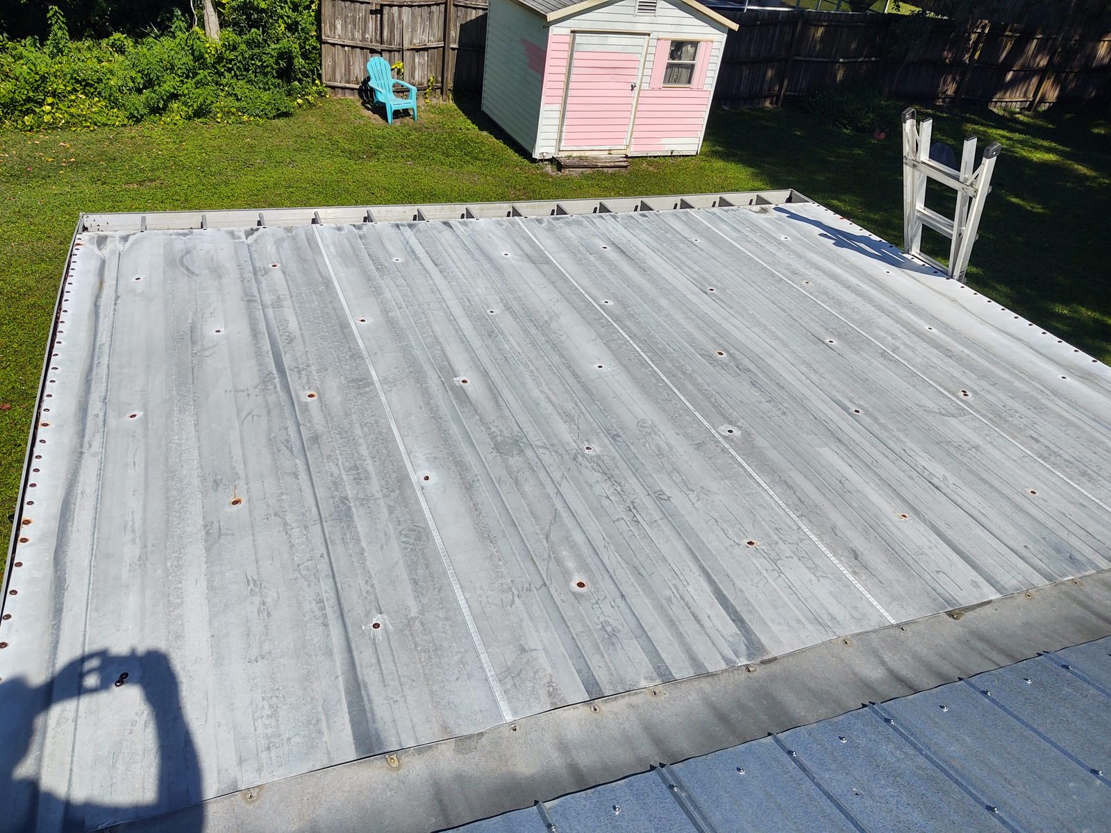 Weathered corrugated metal roof with surface staining and exposed fasteners before any coating