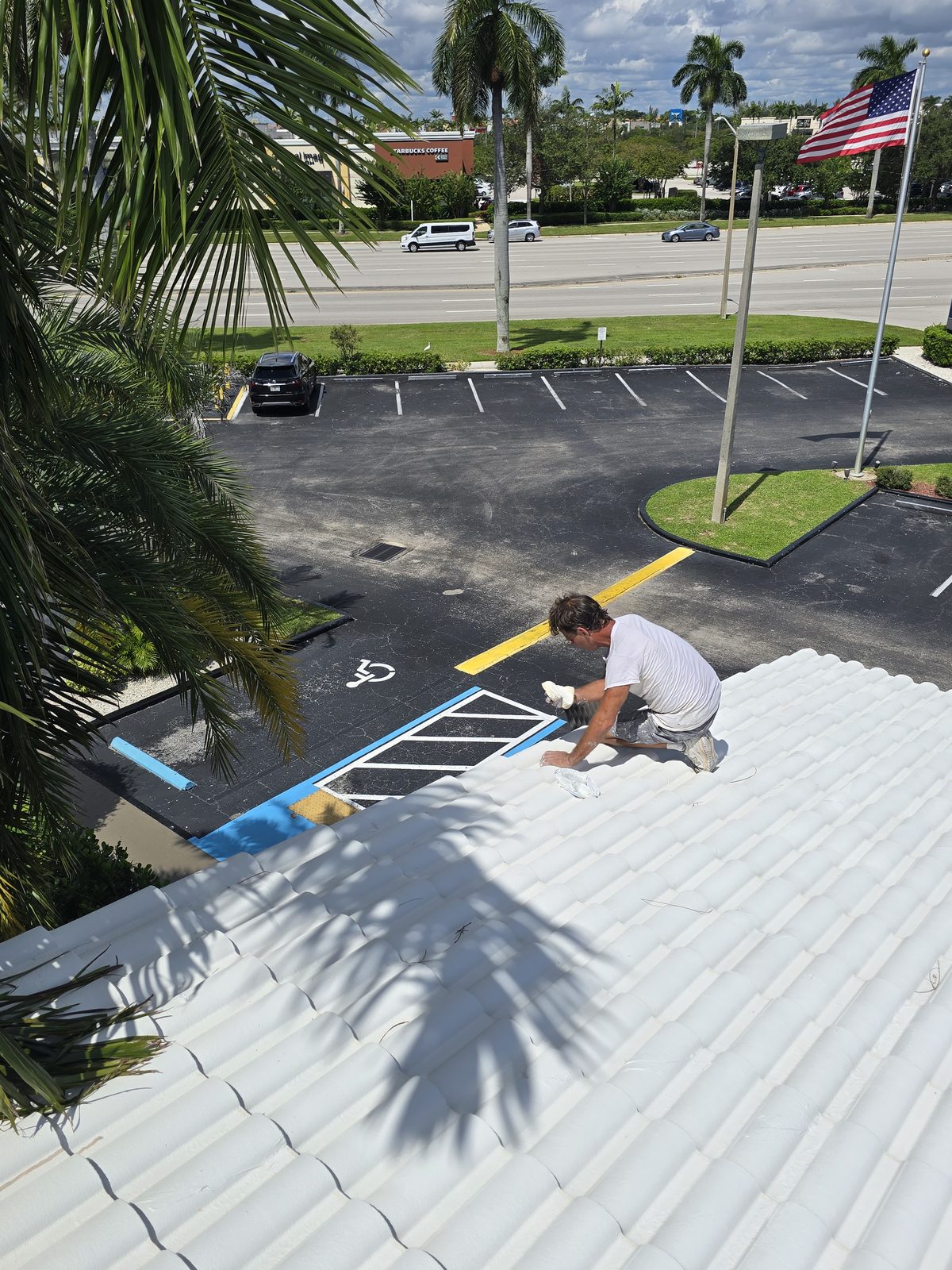 Roofer kneeling on a coated tile roof detailing the edge above a commercial parking lot