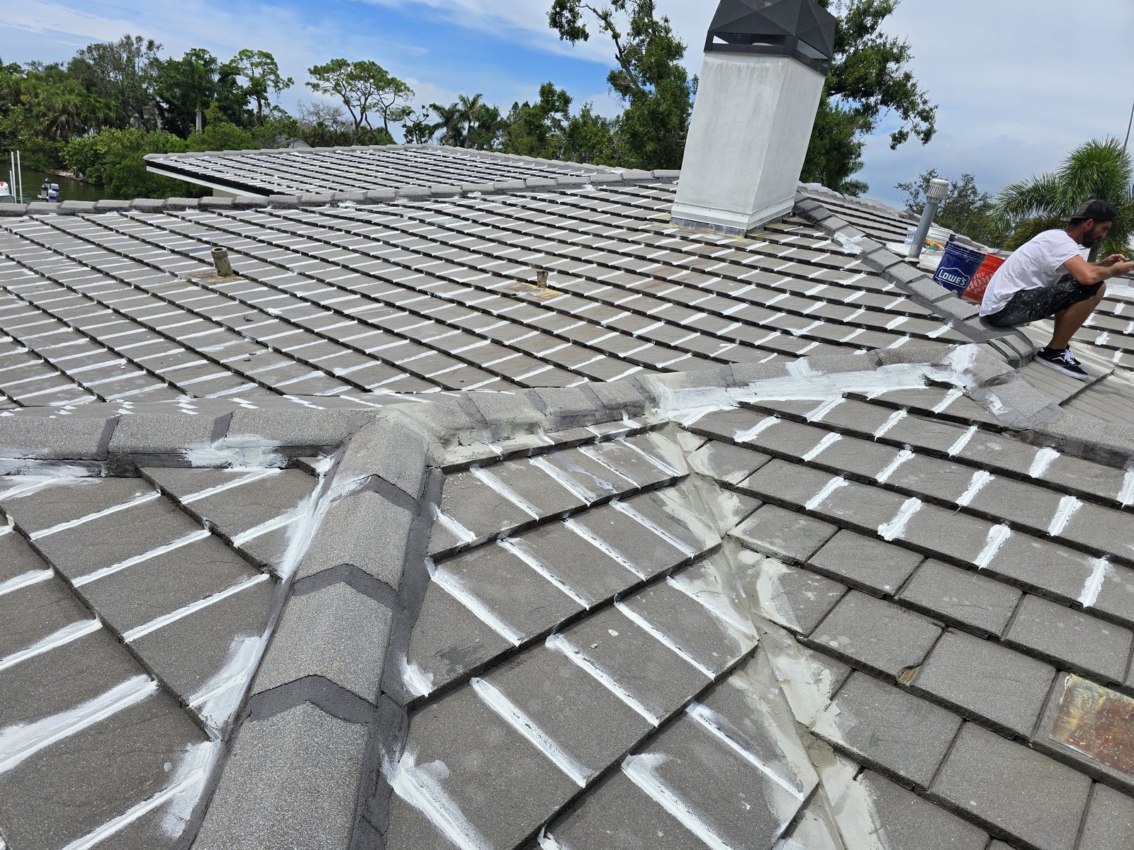 Gray concrete tile roof part-way through coating, sealed joints showing white against untreated tile