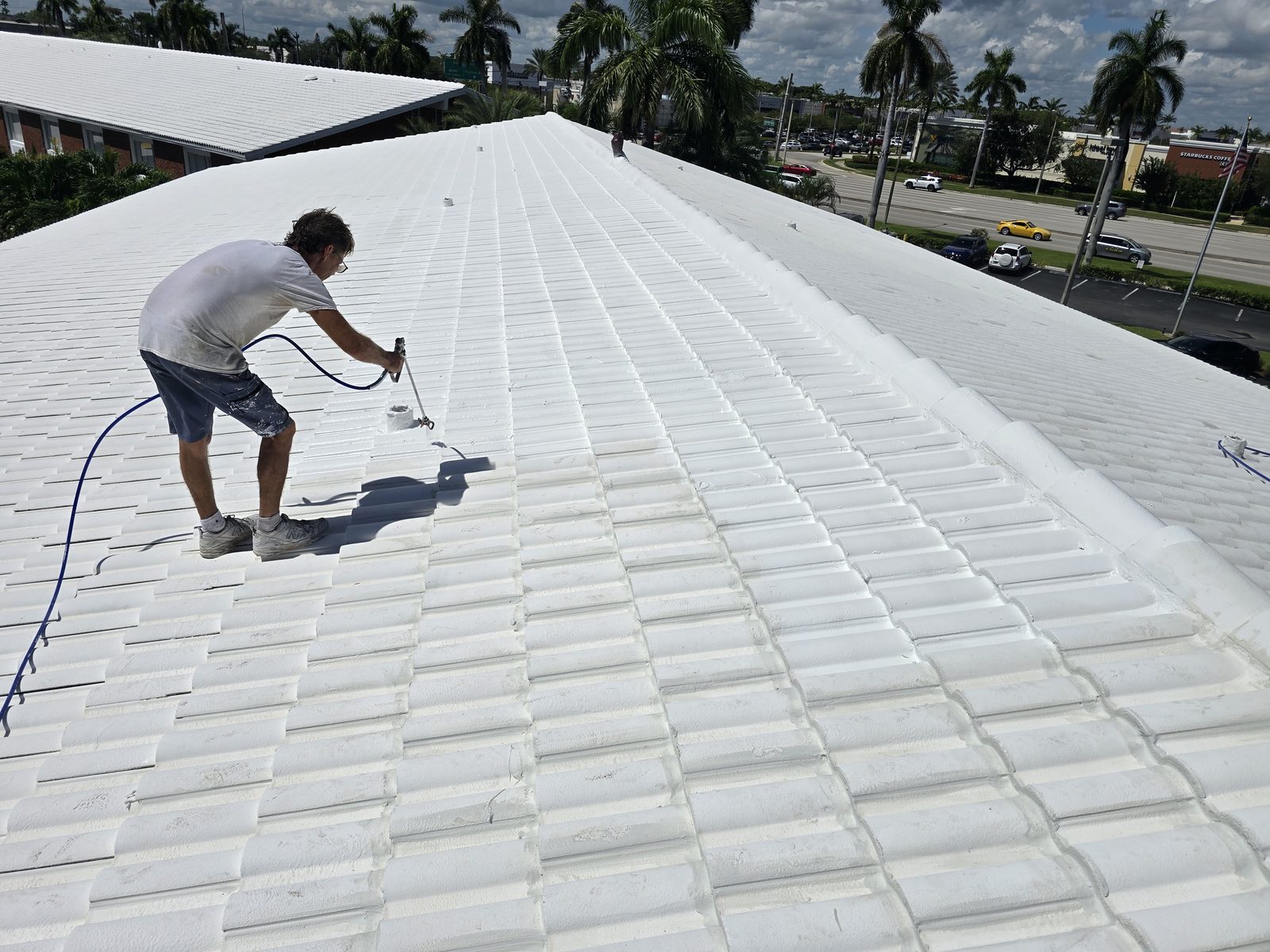 Roofer spray-applying white reflective coating along the length of a concrete tile roof